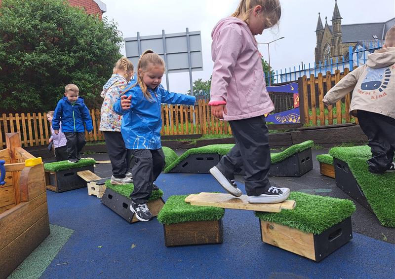 6 children have constructed an oval obstacle course, which contains blocks from the Get Set, Go! set and wooden planks and blocks from a Play Builder set. The children look engaged as they walk through.
